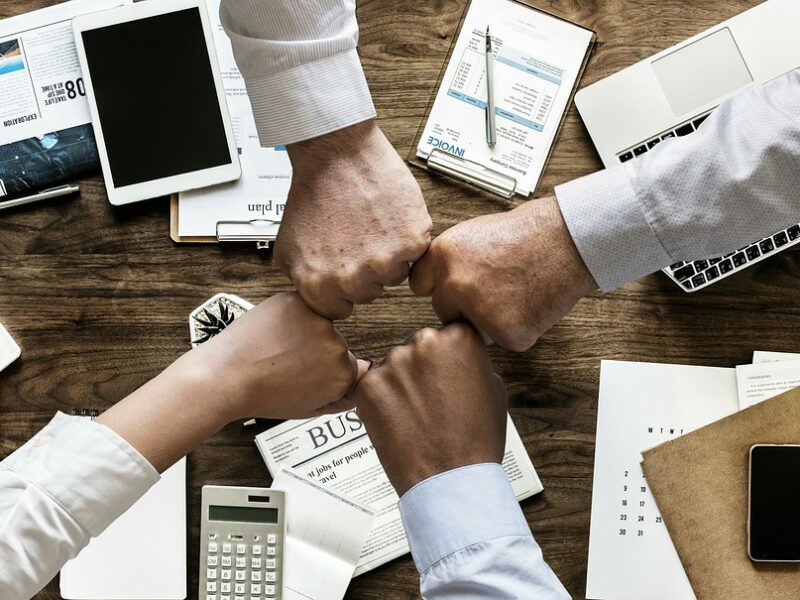 4 people fist-bumping over a table with business papers